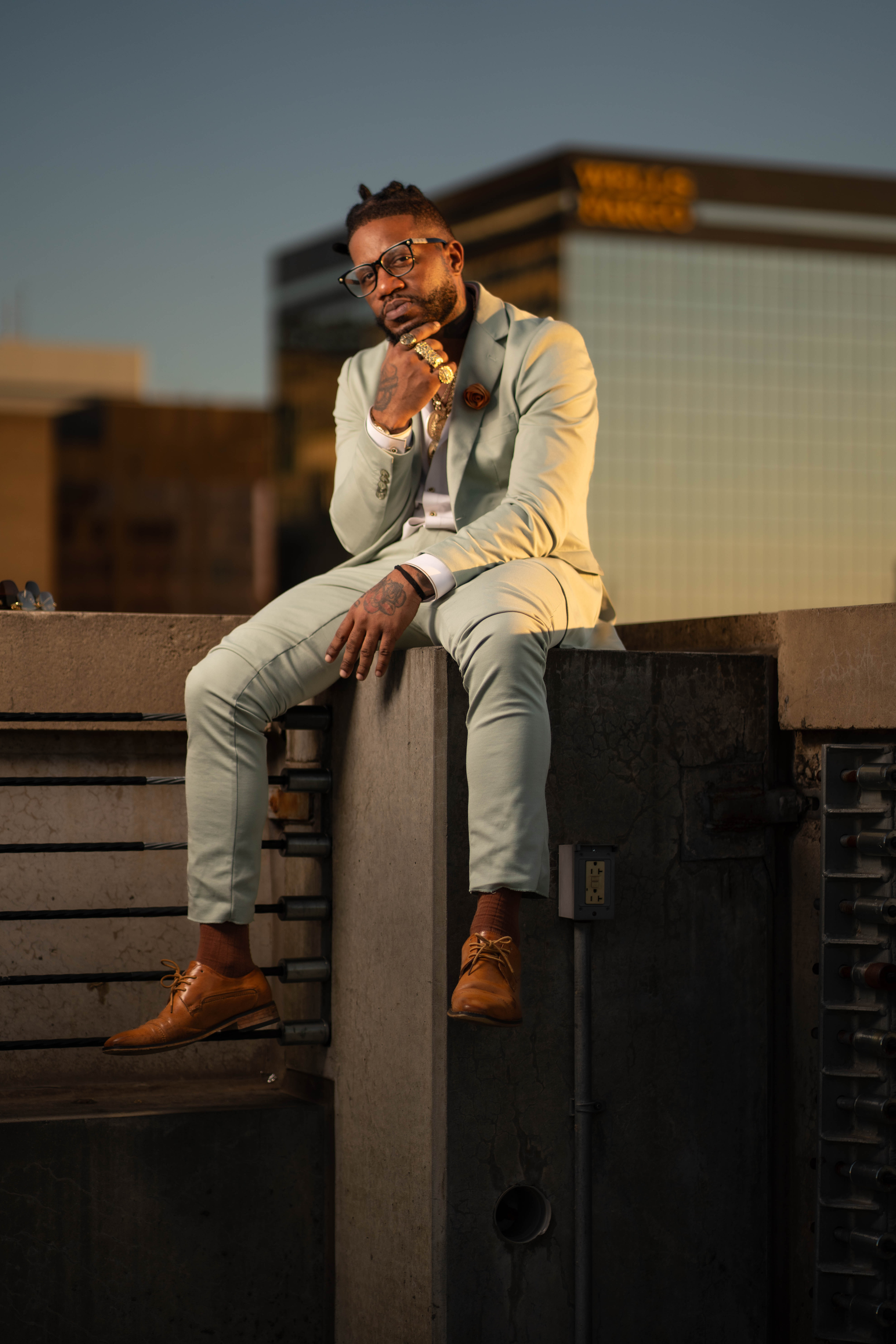 Man in a light suit seated on an outdoor stone ledge.