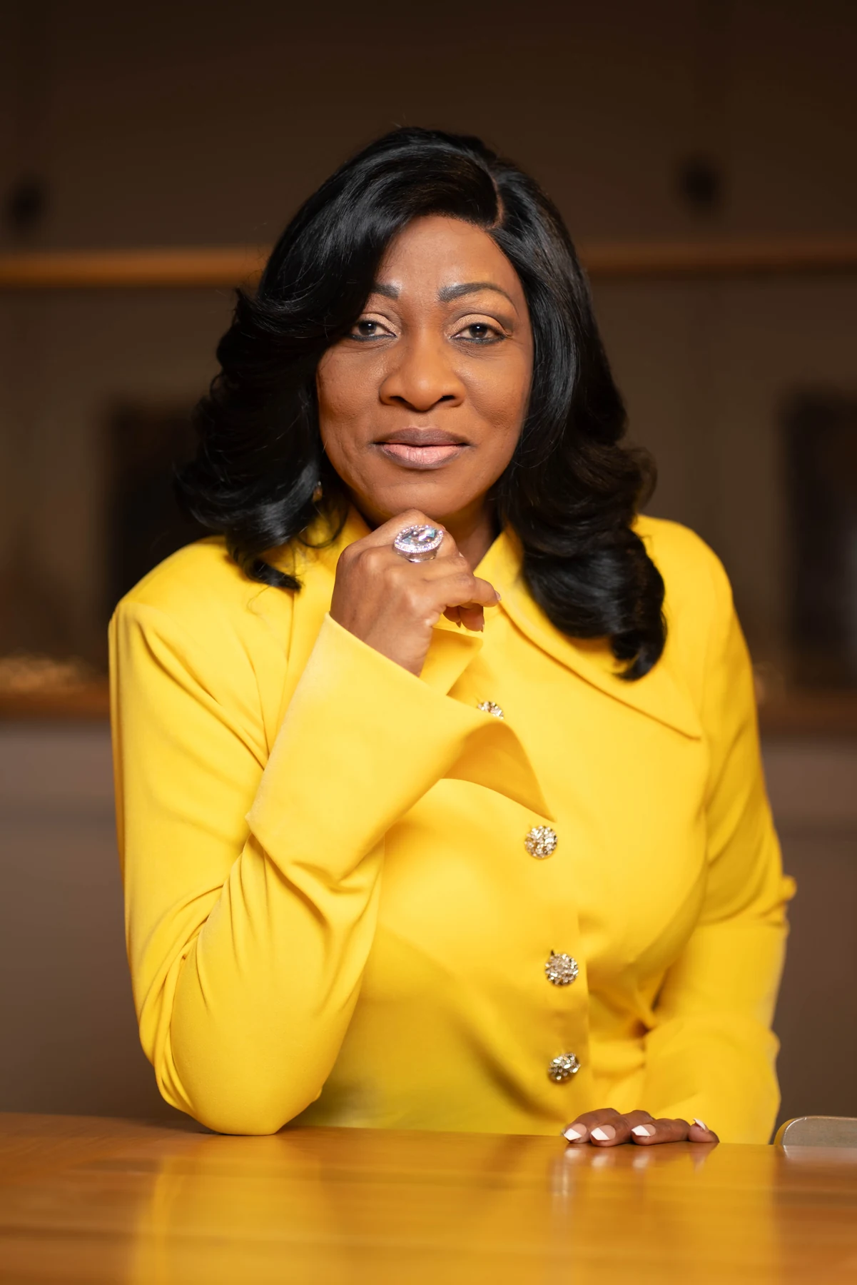 Woman in a yellow blazer resting her chin on her hand.