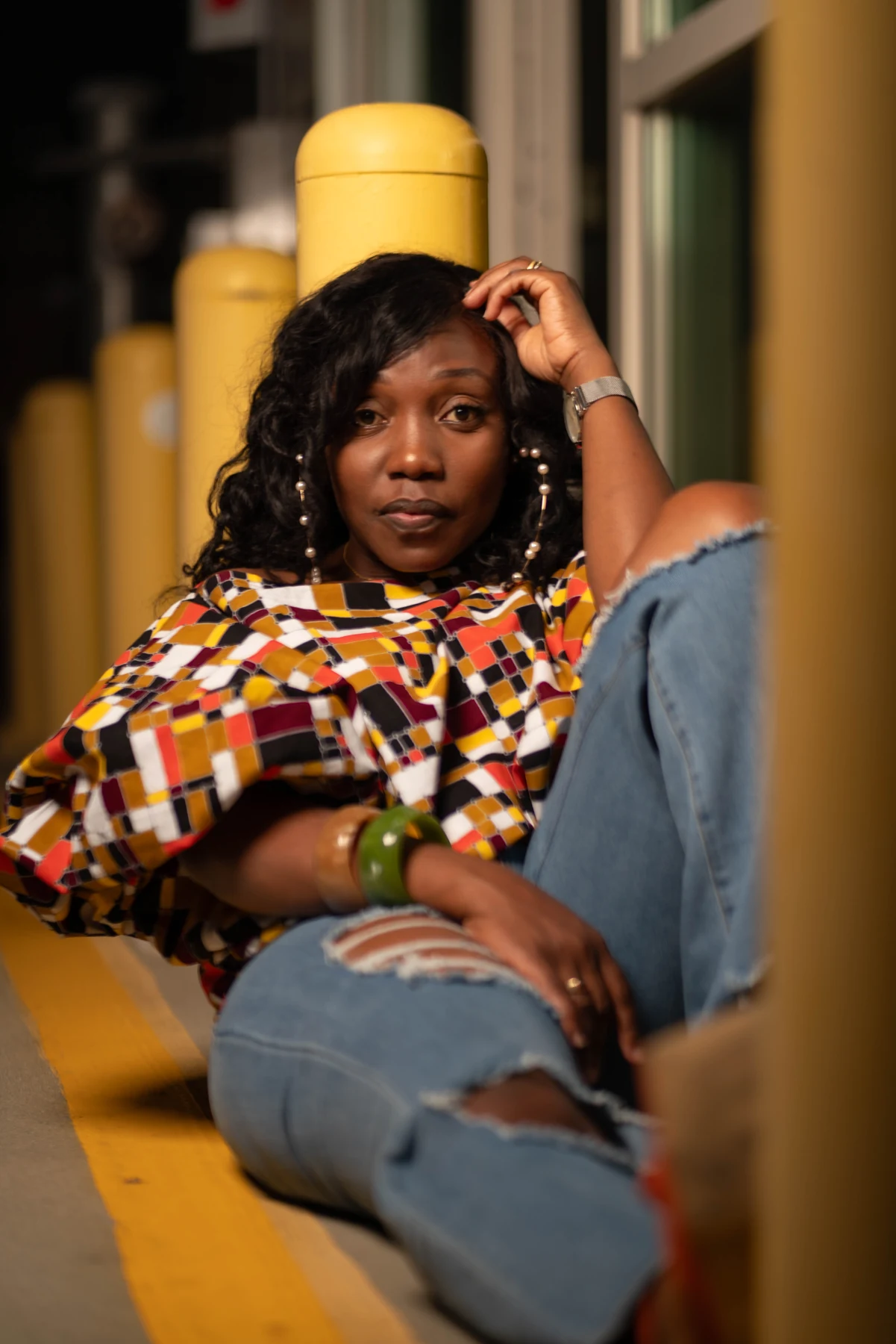 Woman in a colorful patterned blouse seated beside a yellow column.